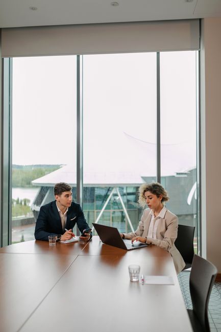 Two professionals engaged in a business meeting with laptops in a modern office setting.