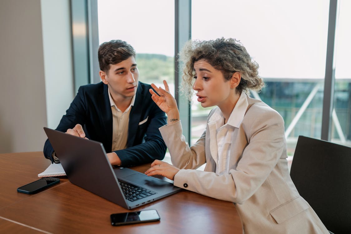 Free Man in Beige Suit Jacket Sitting Beside Woman in Black Blazer Using Macbook Pro Stock Photo