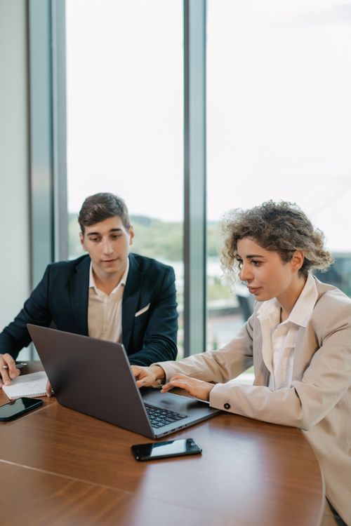 Free Colleagues in business attire working together on a laptop in a modern office setting. Stock Photo