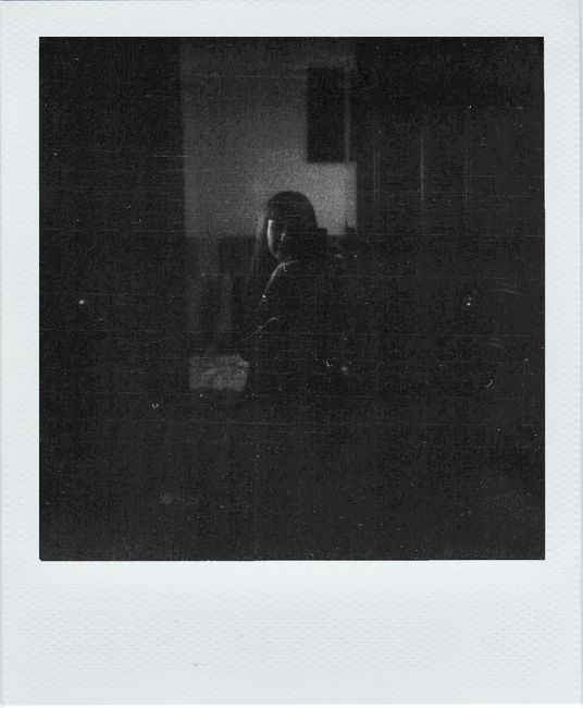 A dark and moody black and white portrait of an unrecognizable woman indoors.
