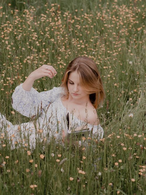 Free Relaxing scene of a woman reading in a serene flower-filled meadow. Perfect summer escape. Stock Photo