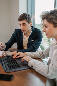 Two young professionals working together on a laptop, discussing projects in a modern office setting.