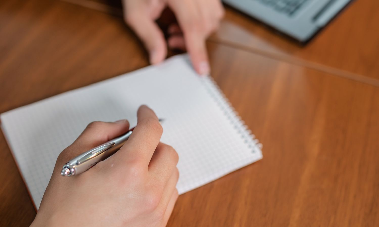 Persona tomando notas con bolígrafo y cuaderno durante una reunión