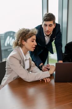 Two professionals in business attire collaborating on a laptop in a modern office setting.