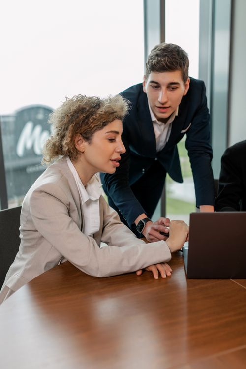 Free Two professionals in business attire collaborating on a laptop in a modern office setting. Stock Photo