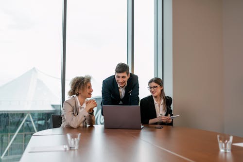 Man in Black Suit Discussing with his Colleagues using Laptop