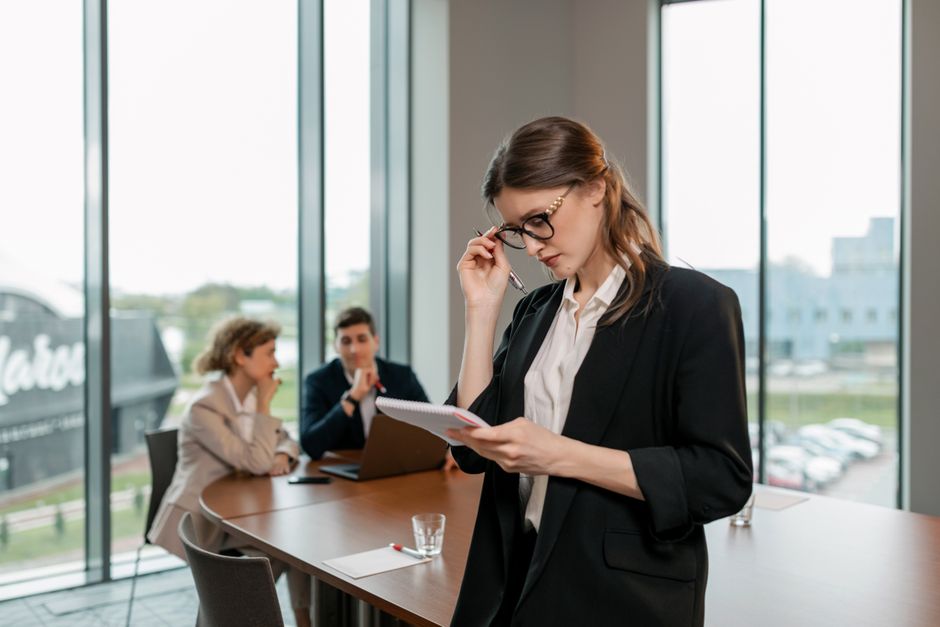 Mujer segura revisando notas mientras lidera una reunión de negocios en un entorno de oficina moderna.