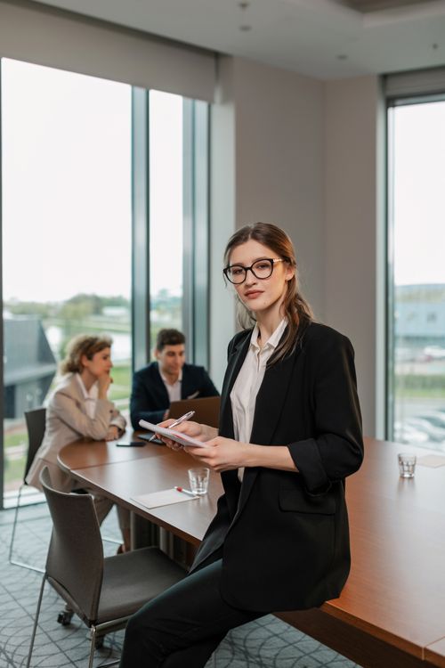 Free Professional woman in a black blazer holding a notebook in a modern office setting. Stock Photo