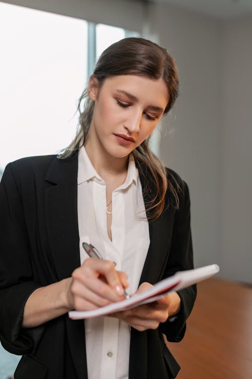 Woman in Black Blazer Standing while Writing Notes
