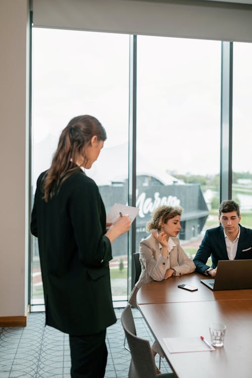 Free Woman in Black Blazer Standing in Front of a Woman and Man Using Laptop Stock Photo