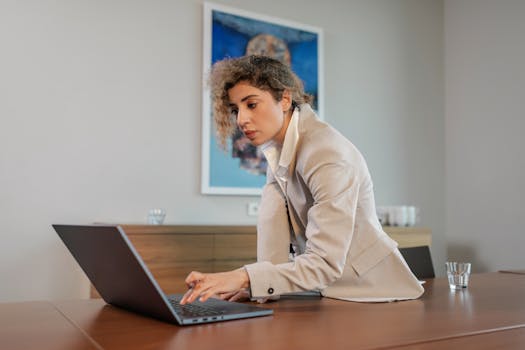 Businesswoman in a beige blazer working on a laptop at a modern office desk.