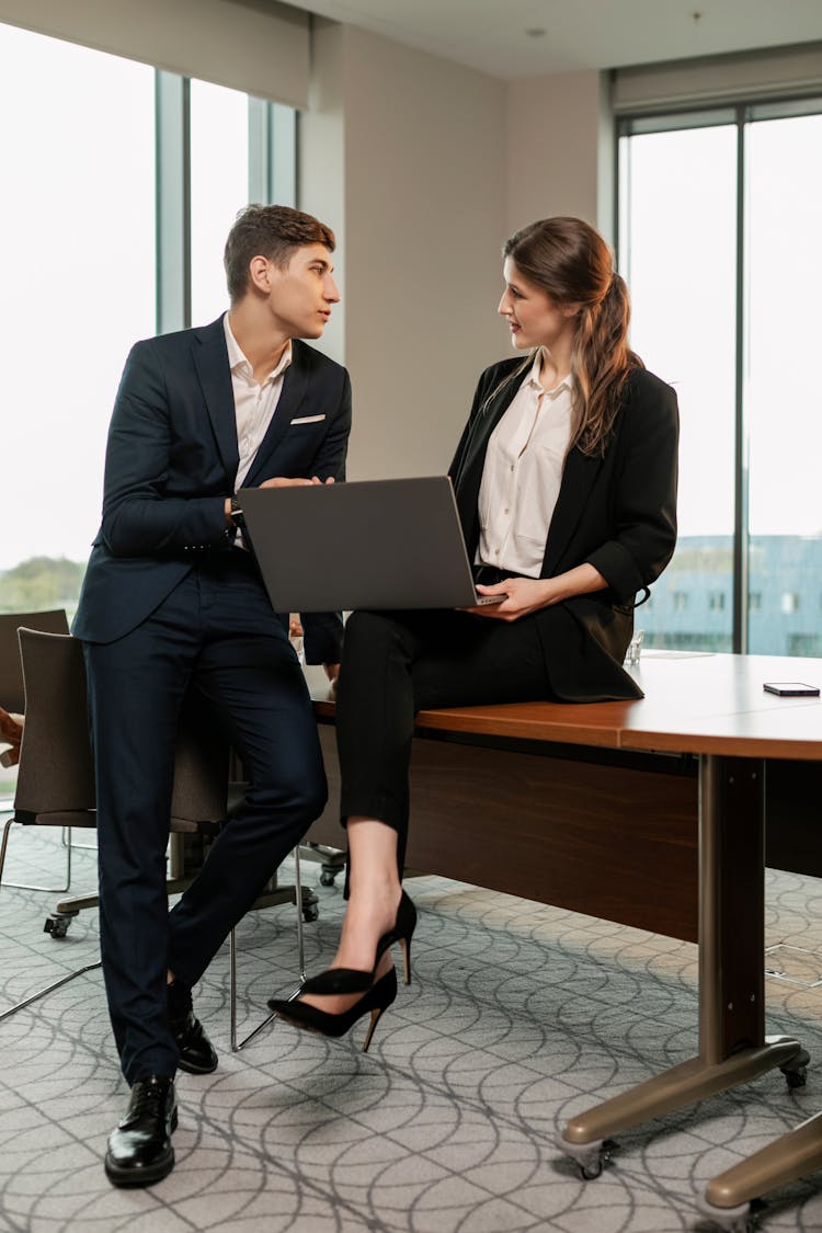 Woman Sitting On Wooden Table While Talking To A Man In Blue Suit