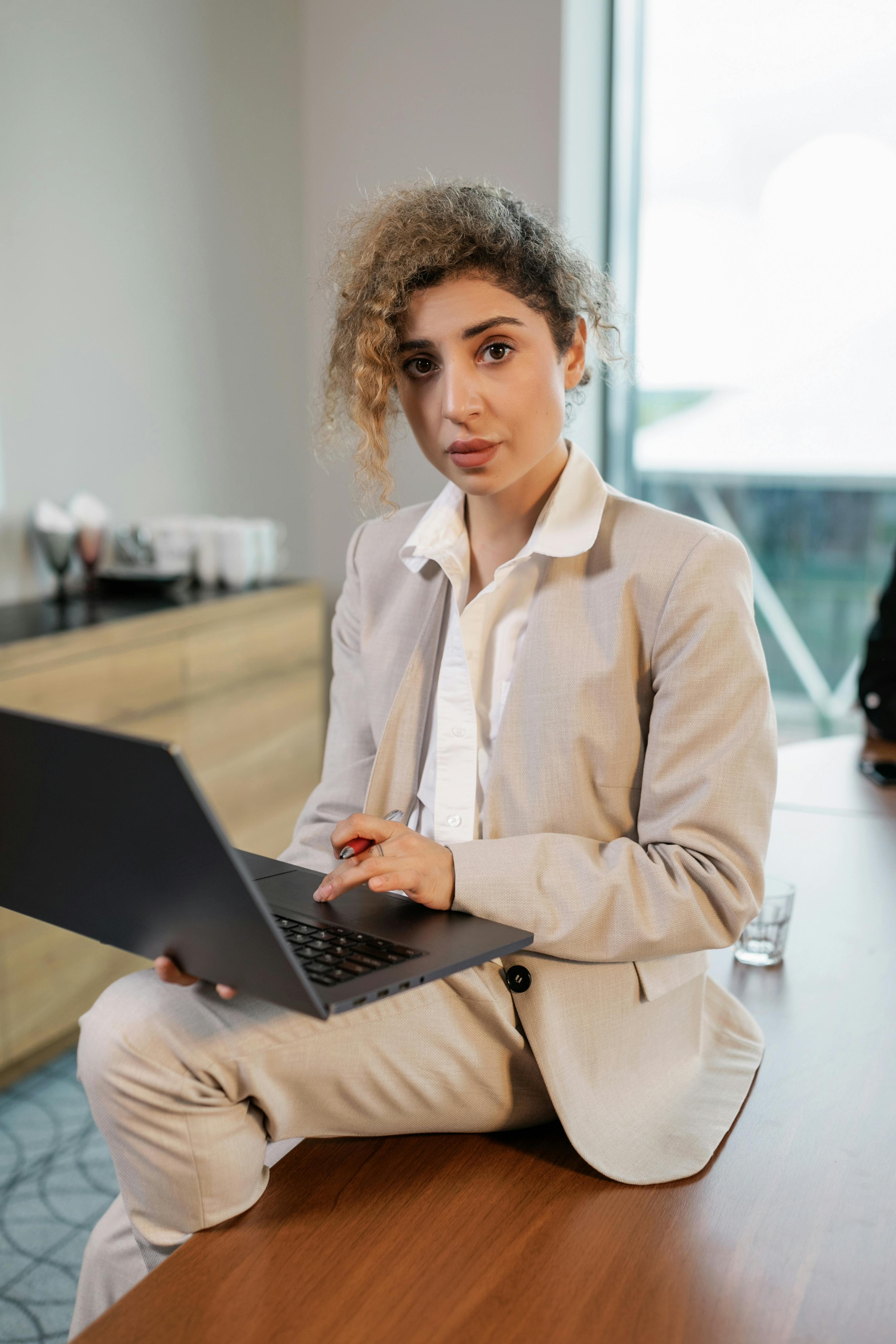 woman in beige blazer sitting on table using laptop computer
