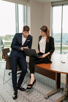 A man and woman collaborate on a project in a corporate office with a laptop.