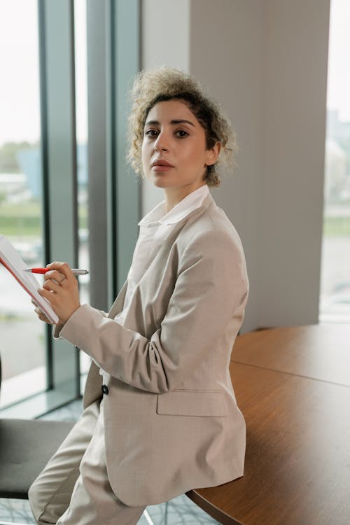 Free Woman in Beige Blazer Holding a Pen and Notebook Stock Photo