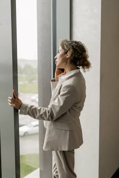 Confident businesswoman in formal attire making a phone call by the window indoors.