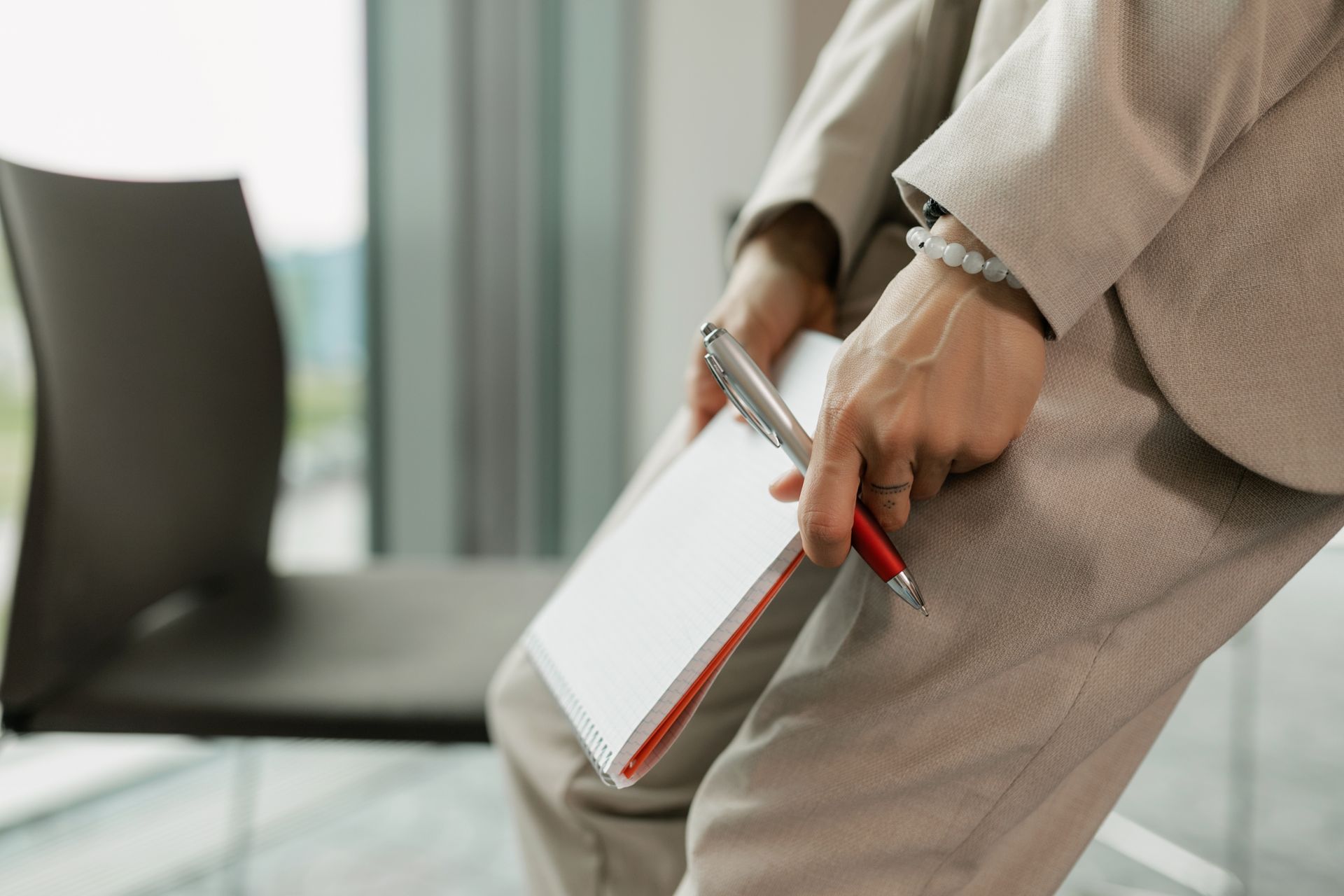 Business professional holding a notebook and pen wearing beige suit indoors.