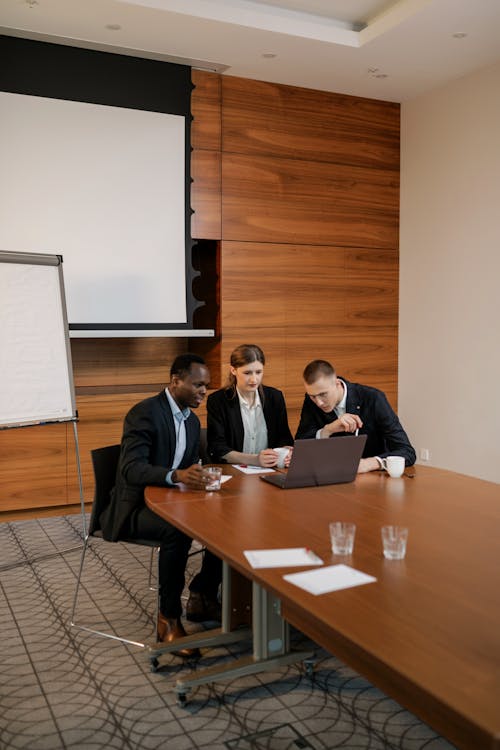 A Group of People Sitting Near the Wooden Table while Looking at the Laptop