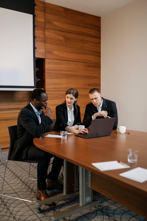 A Woman Talking to Her Colleagues while Sitting Near the Wooden Table