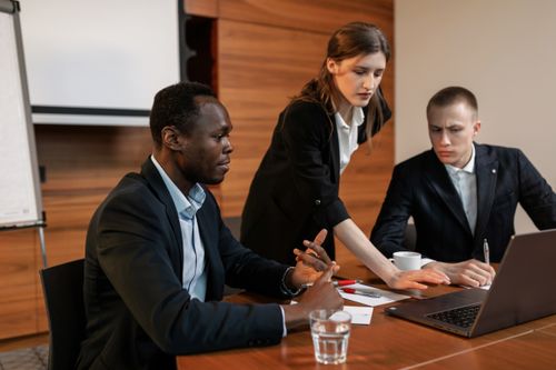Free Business team engaged in a collaborative meeting around a wooden table in a modern office setting. Stock Photo
