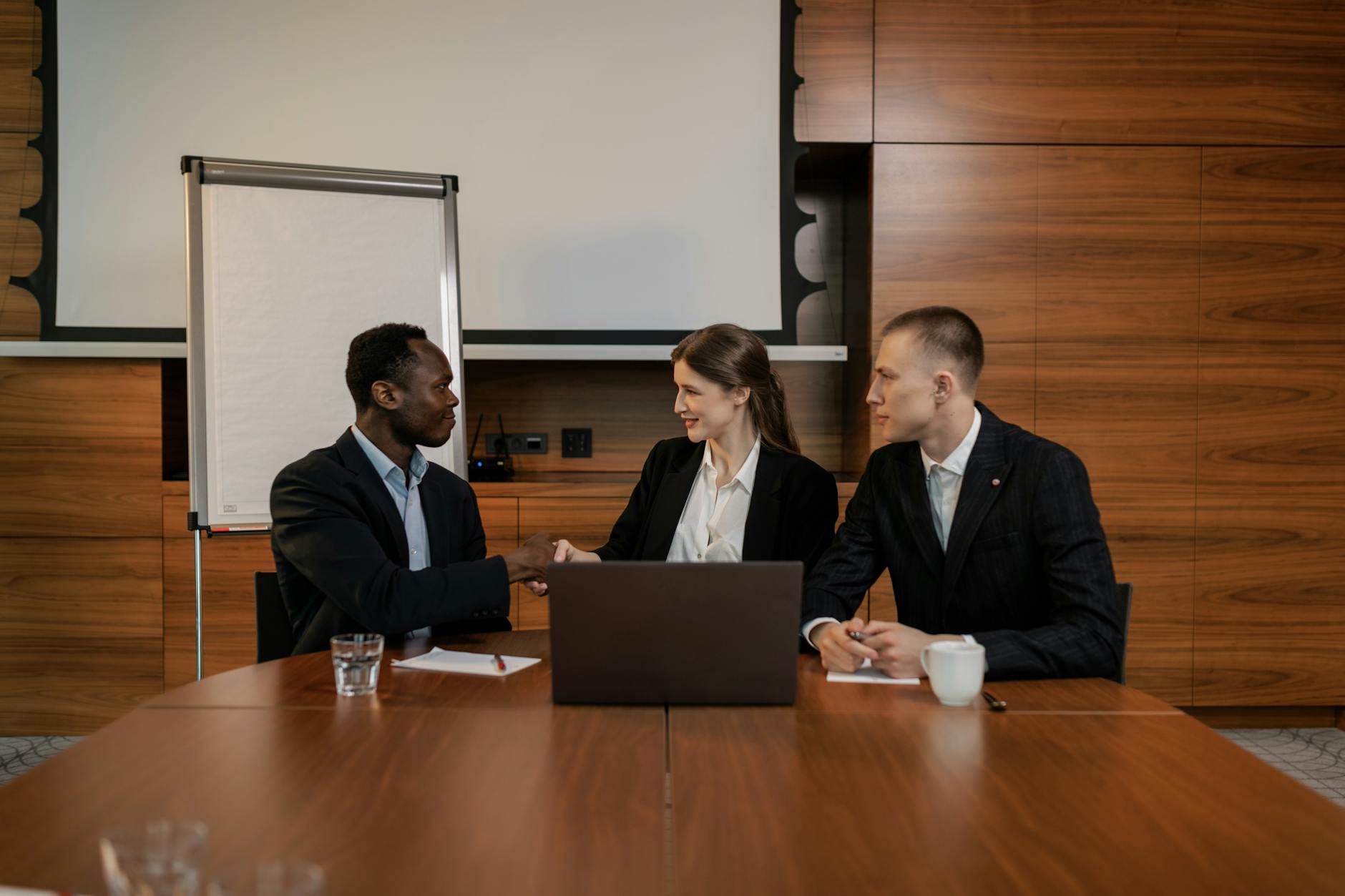 A diverse group of professionals engaged in a business meeting, collaborating and shaking hands in an office setting.