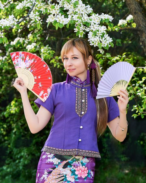 Free A woman in traditional clothing holding two hand fans under blooming spring trees. Stock Photo