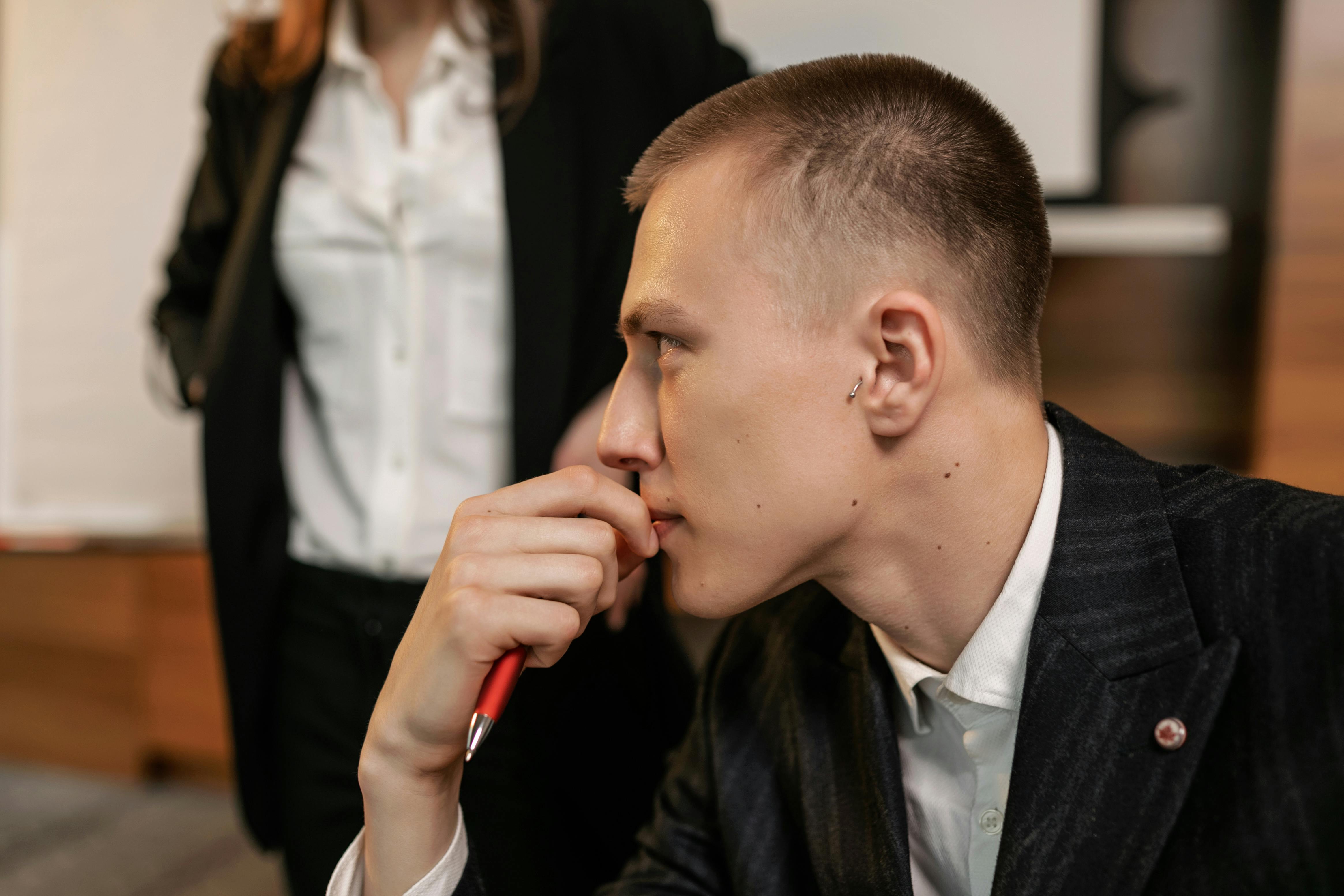 Side view of a thoughtful businessman holding a pen, contemplating in a modern office.