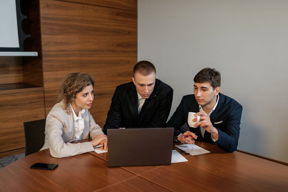 Três profissionais colaboram em um ambiente de escritório moderno focados em um laptop.