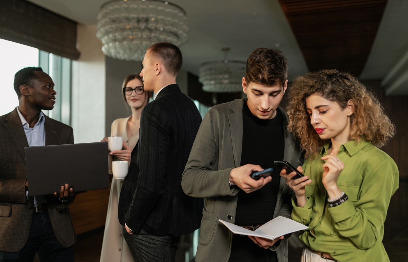 Group of diverse business professionals networking indoors with smartphones and coffee.