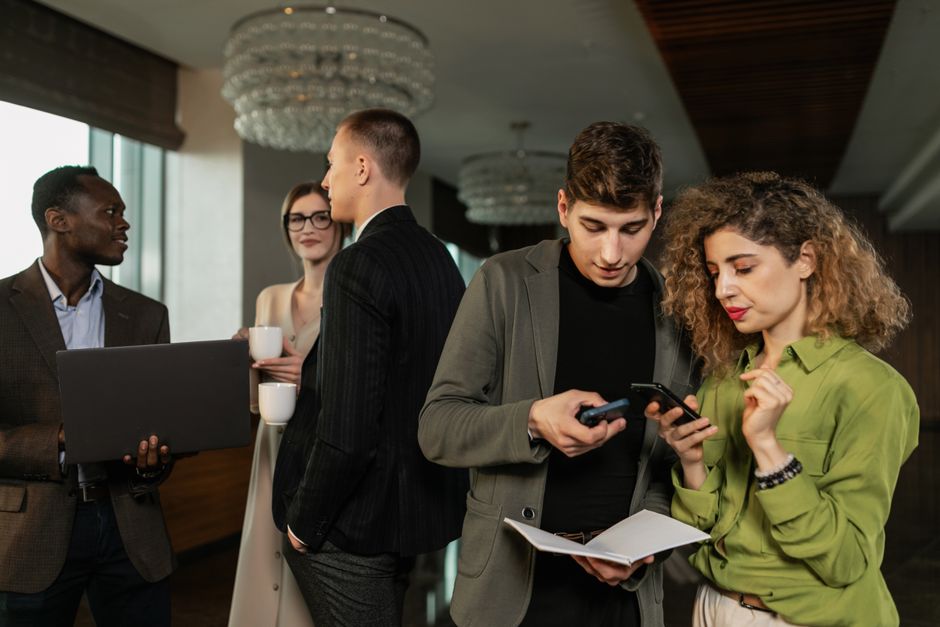 Group of diverse business professionals networking indoors with smartphones and coffee.