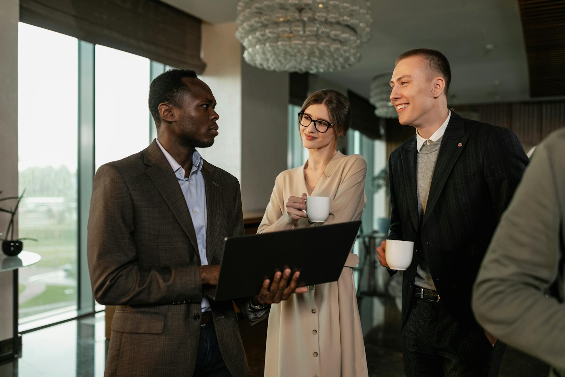 Man in Brown Business Suit Holding Black Laptop while Standing