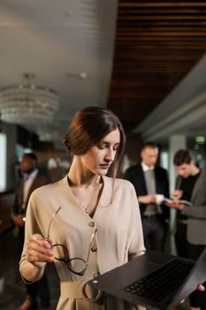 A focused businesswoman holding a laptop in a contemporary office environment.