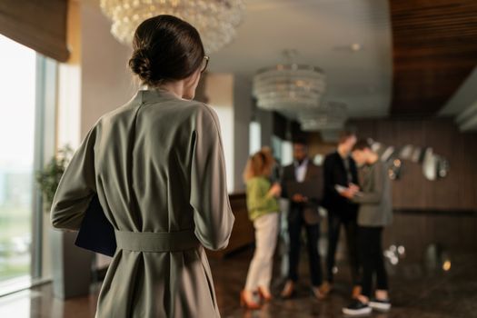Backview of a focused woman observing colleagues discussing in a modern office lobby.