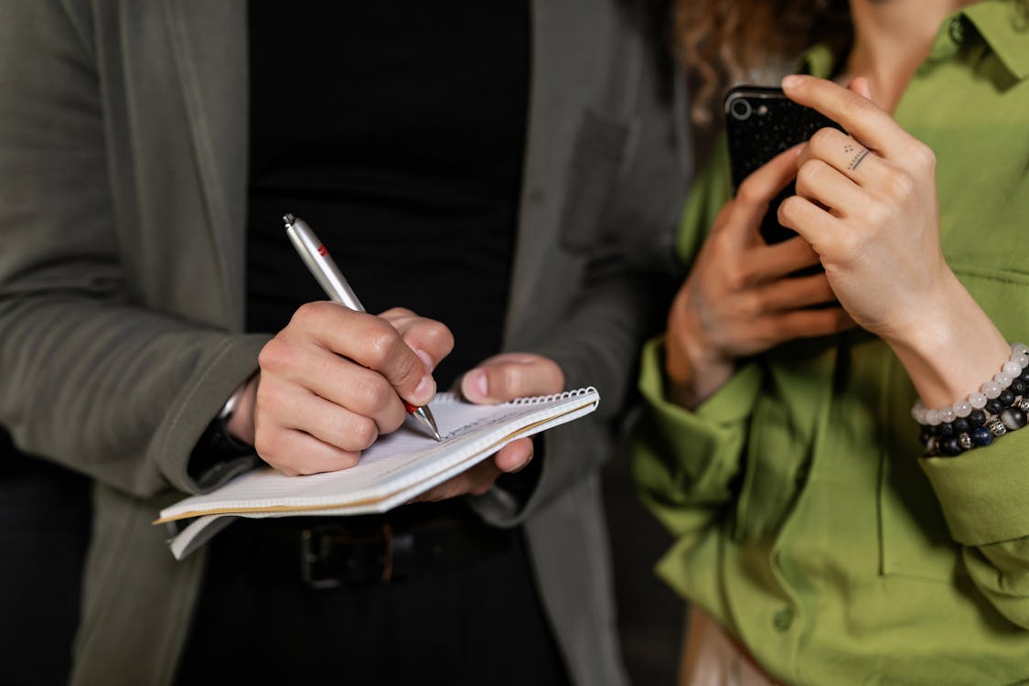 Free Person in Green Jacket Holding Black Smartphone Stock Photo