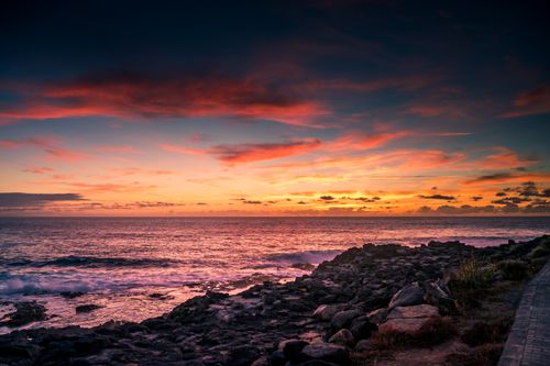 Free A vibrant sunset view over a rocky seashore with colorful skies and ocean waves. Stock Photo