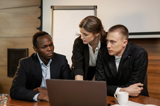 Multi-ethnic team discussing project around a laptop in an office setting.