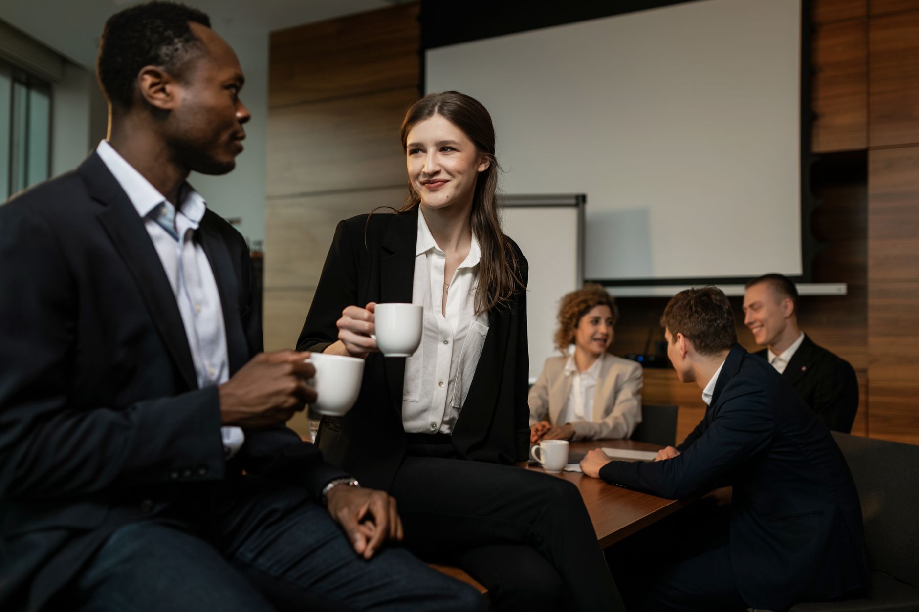 Grupo de profissionais diversos disfrutando de uma pausa para café durante uma reunião de negócios em uma sala de conferência.