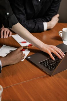 Close-up of diverse hands working on a laptop in a collaborative office setting.