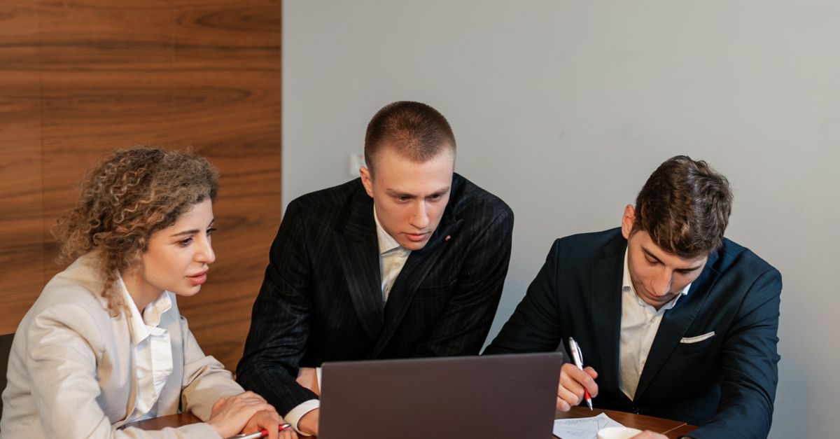 Photo by Alena Darmel Collaborative business meeting with three professionals focused on a laptop in a modern office.