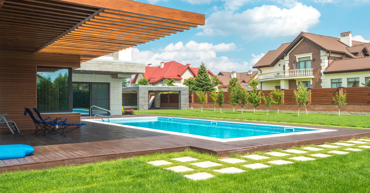 Stunning modern home exterior with a pool and well-maintained backyard under a blue sky.
