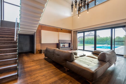 Spacious living room featuring a leather couch and wooden flooring with outdoor pool access.