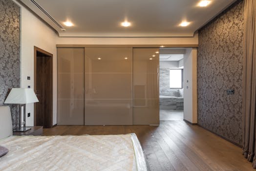 Spacious modern bedroom featuring minimalist design, elegant wallpaper, and warm lighting.