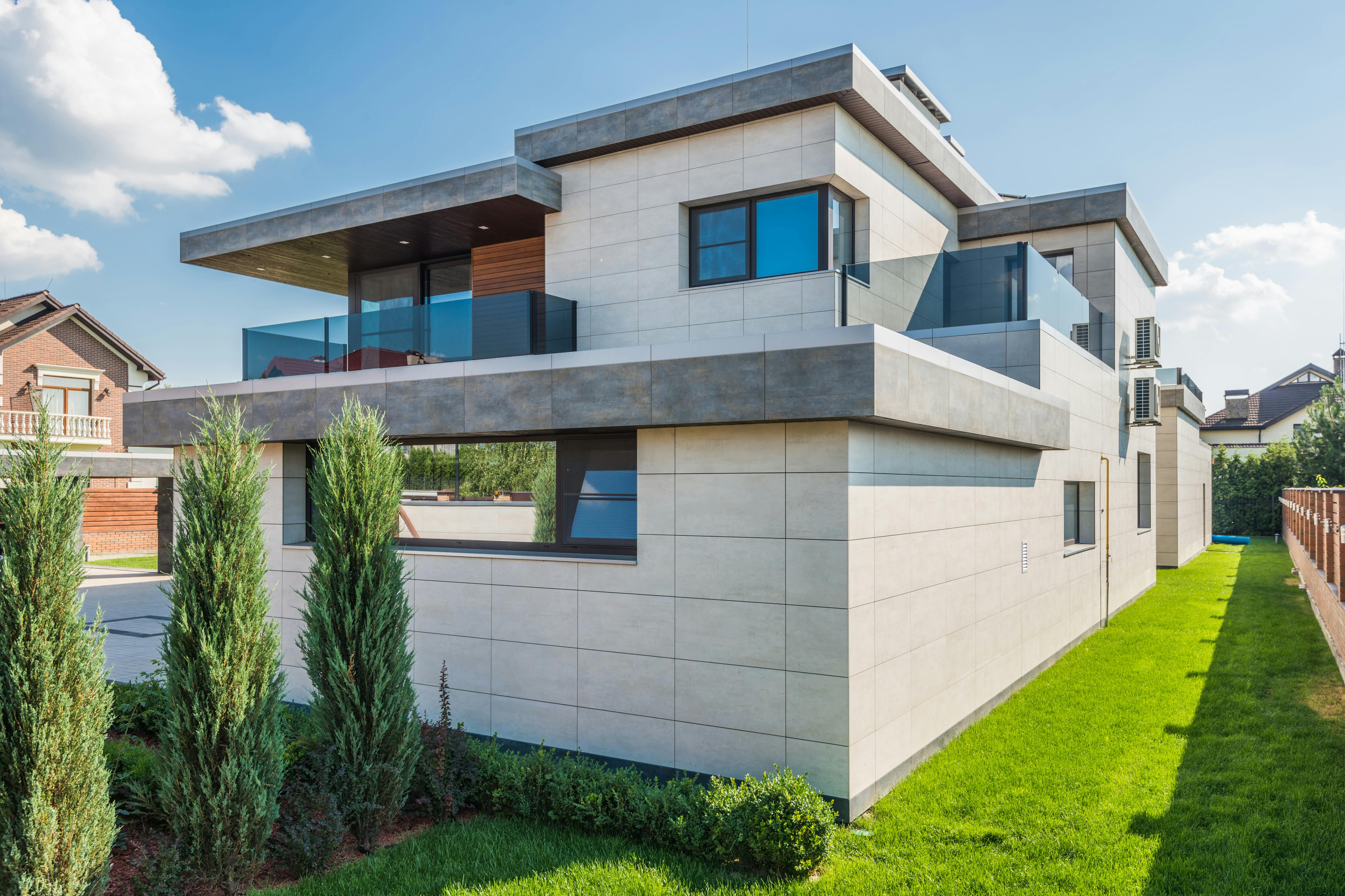 a modern house near the green grass with green plants under the blue sky