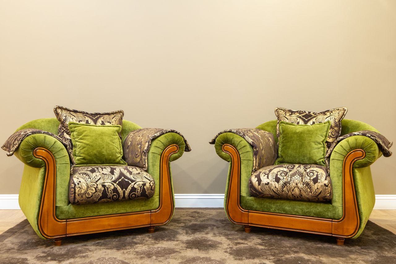 two vintage green armchairs with ornate cushions set against a beige w