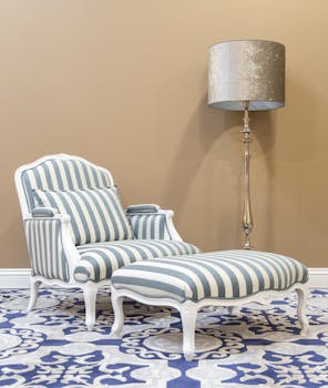 Elegant striped armchair and footrest with a classic floor lamp in a cozy interior setting.