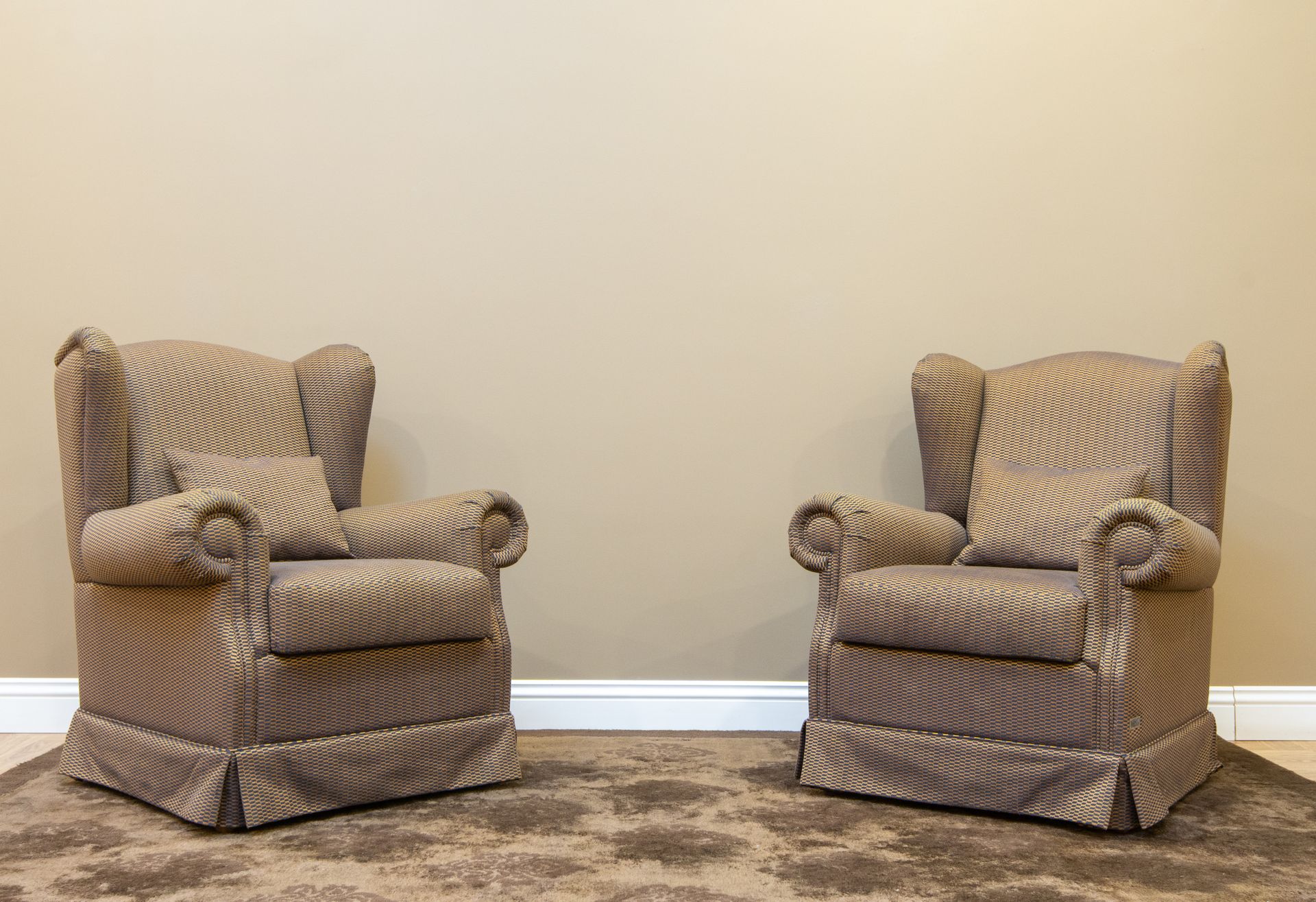 Pair of beige wingback armchairs with pillows in a classic studio setting.