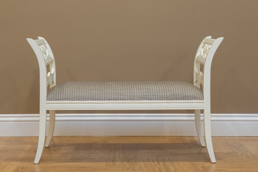 A classic white wooden bench with upholstered seat against a beige wall, perfect for stylish interiors.