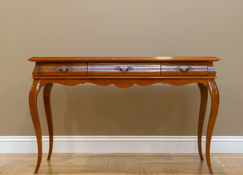 Classic wooden console table with elegant design and metal handles against a beige wall.