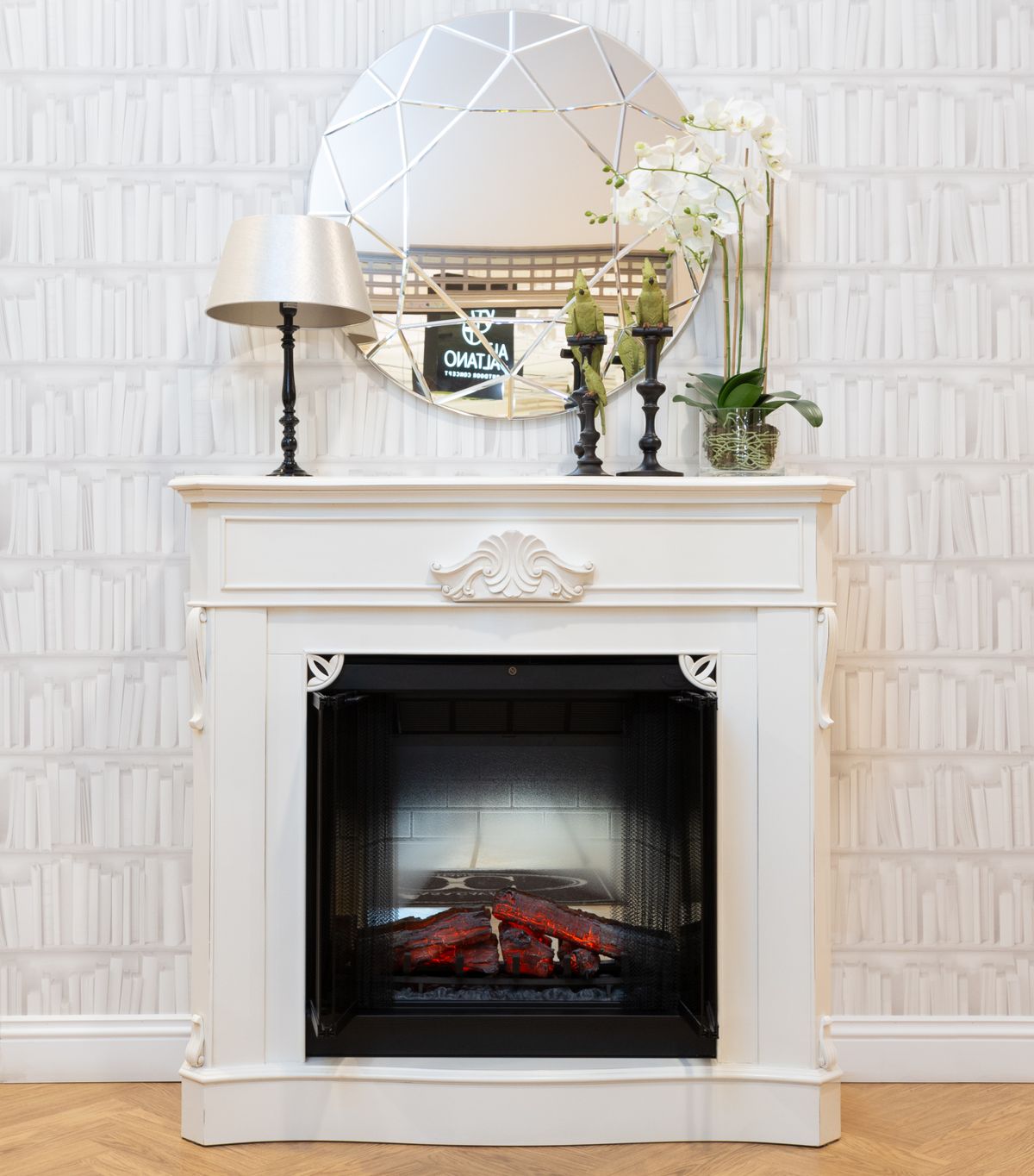 A stylish white fireplace with a decorative mantel, mirror, lamp, and candlesticks in a cozy interior. Stock Photo.