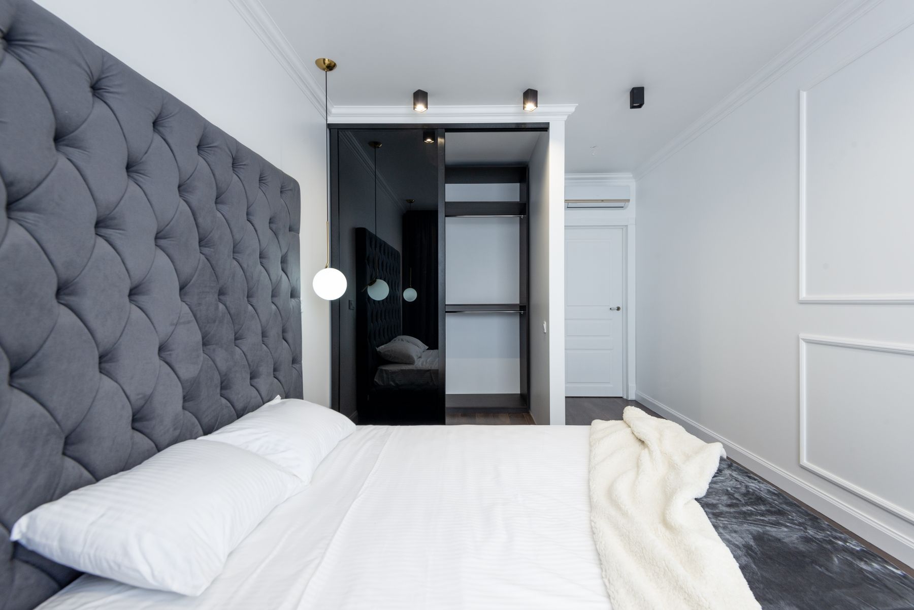 Bedroom with a broad upholstered headboard aligned to bedside furniture and an open wardrobe
